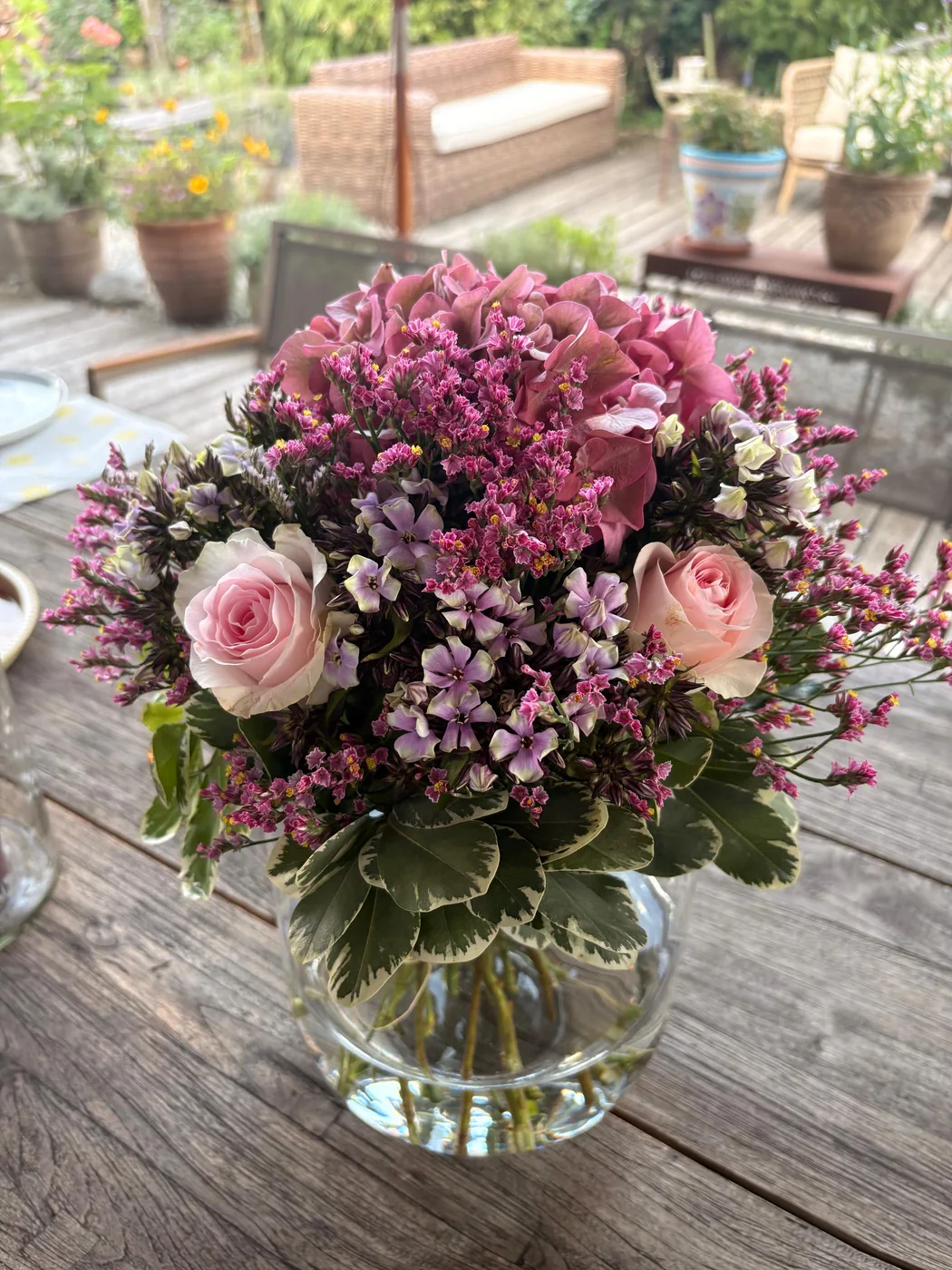 Sommerstrauß mit Hortensie, Rosen und Statice in der Kugelvase auf dem Gartentisch
