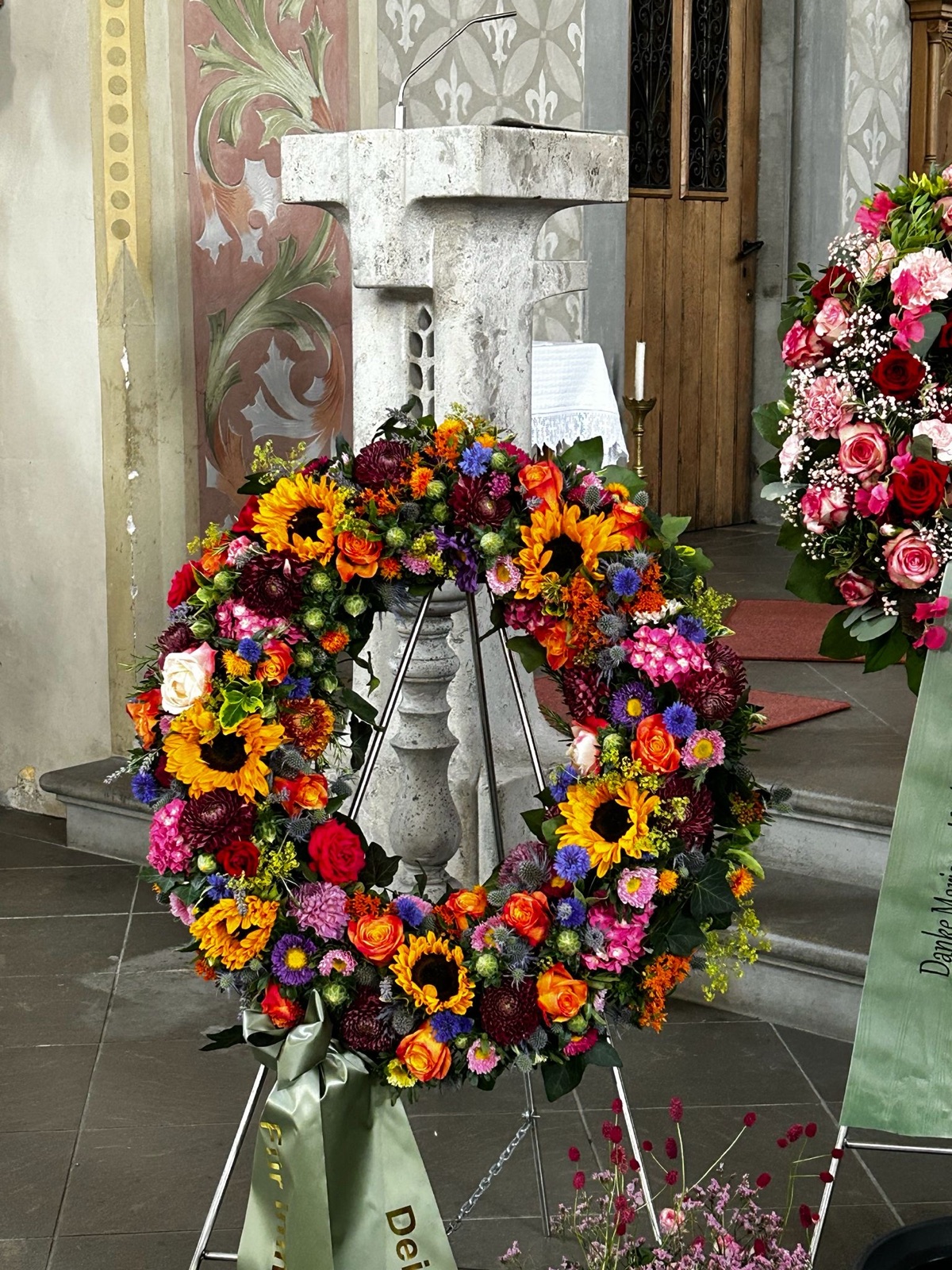 Farbenfroher Trauerkranz mit Sonnenblumen und Rosen in der Kirche