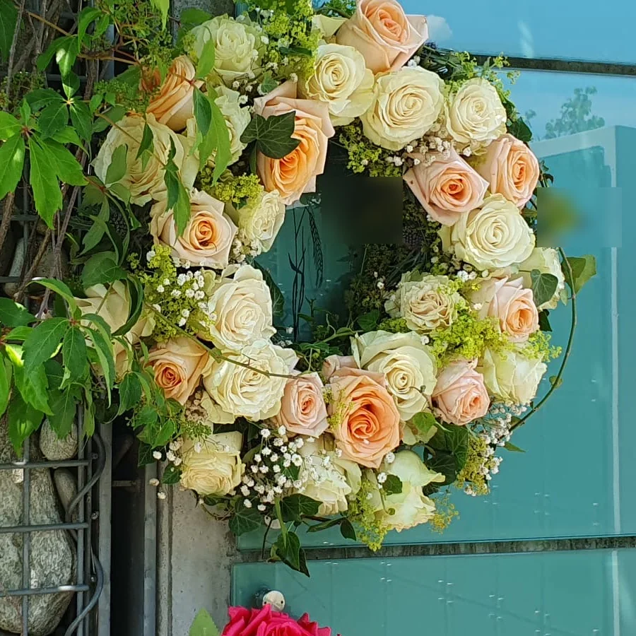 Trauerkranz aus cremefarbenen und apricotfarbenen Rosen an der Urnenwand