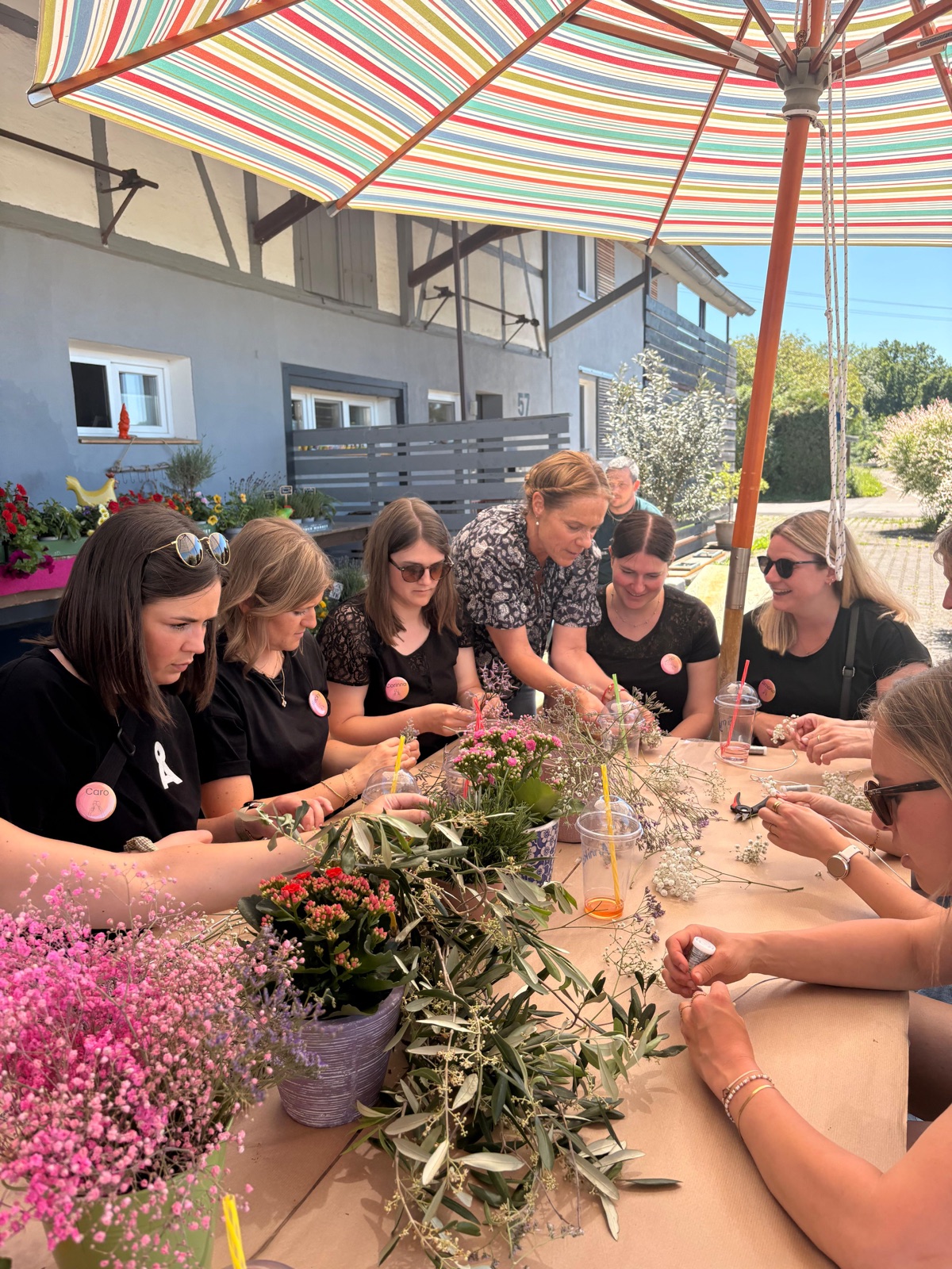 Gruppe beim Kränzebinden als Gruppenevent unterm Sonnenschirm vor dem Laden